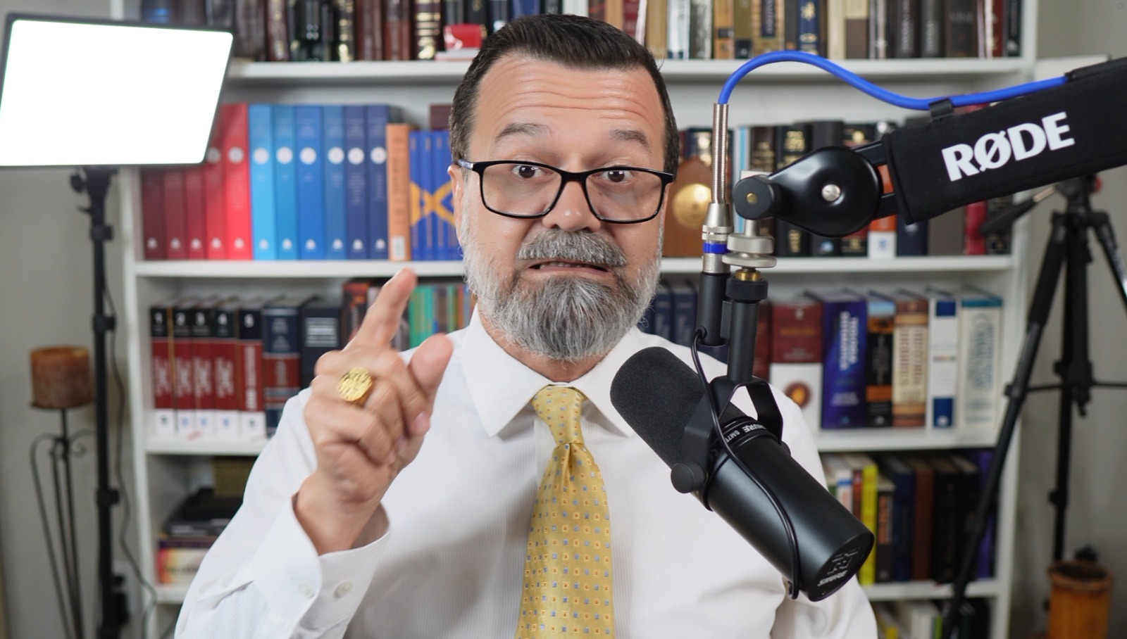 Pr. Moisés Campos dando aula no estúdio, diante da biblioteca